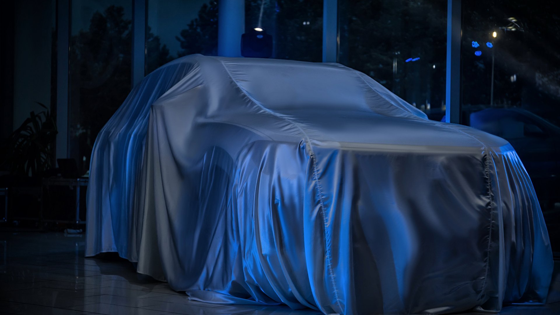 A car covered with a silky fabric in a showroom, ready for unveiling during a car launch event.